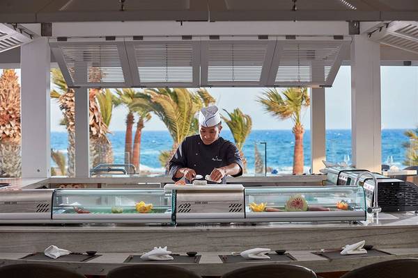 Ein Koch bereitet Sushi in einer Glasfalle im Mare Ayia Napa Hotel zu, mit Blick auf das Meer.