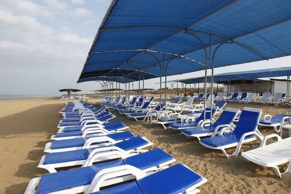 Strand des Cenger Beach Resort & Spa mit vielen blauen Sonnenliegen unter großen blauen Sonnenschirmen.