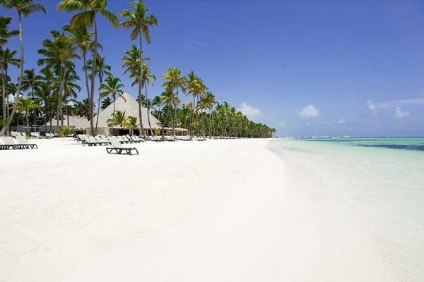 Strand mit weißen Palmen, Sonnenliegen und einem Hotel im Hintergrund