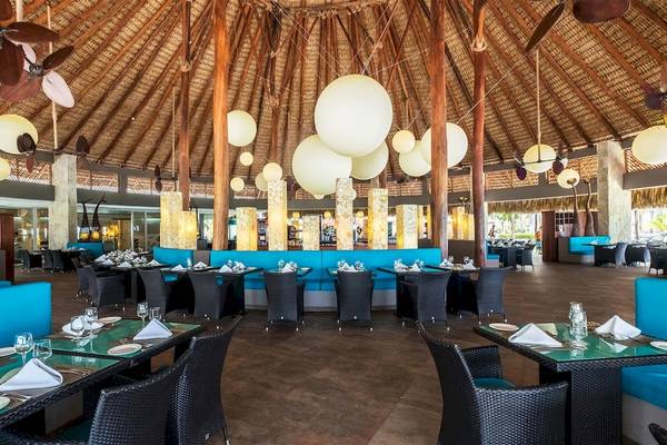 Innenbereich des Barcelo Bavaro Beach Hotels mit blauen Sofas und Tisch, weiße Deckenleuchten und Holzstützen.