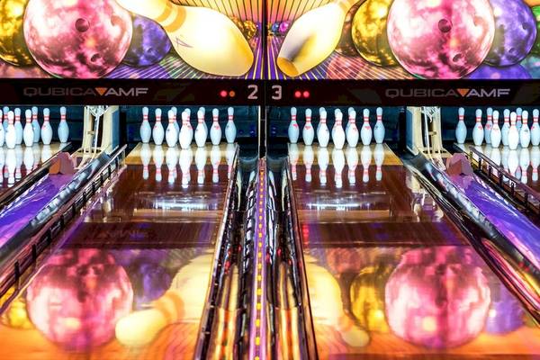 Eine Bowlingbahn mit bunten Bowlingkugeln und Kegeln, bunt beleuchtet.