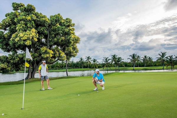 Zwei Golfspieler auf dem Platz vor einem See, einer wirft einen Ball.