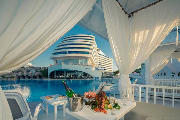 Tisch im Hotelpool-Loungebereich mit Getränken und Essen, Titanic Deluxe Lara im Hintergrund.