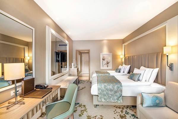 Modernes Hotelzimmer im Titanic Deluxe Lara mit zwei Betten, Schreibtisch und großem Spiegel.