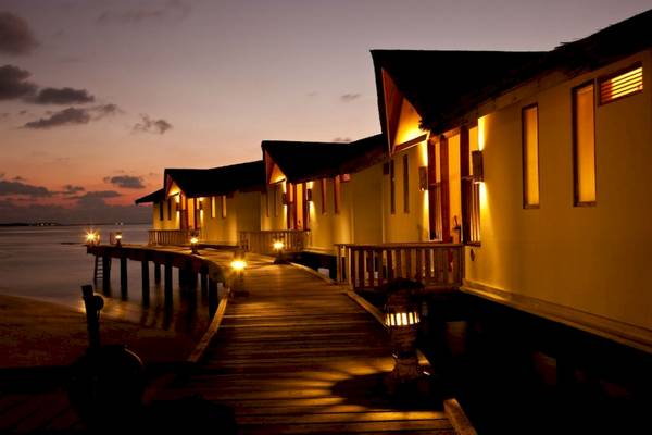 Reethi Beach Resort bei Nacht mit illuminierten Wasserbungalows und leuchtenden Laternen am Steg.