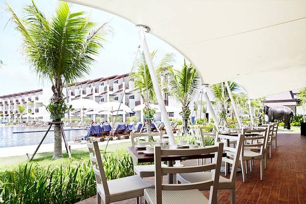 Außenbereich des Sunwing Kamala Beach Hotels mit Tischen und Stühlen, Palmen und Swimmingpool.