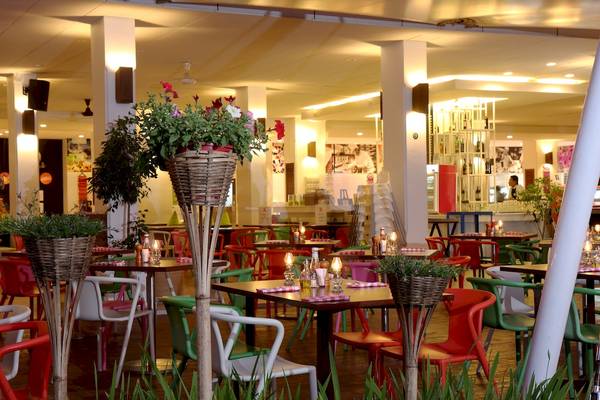Innenansicht des Sunwing Kamala Beach Restaurants mit bunten Tischen und Stühlen, Kerzen auf den Tischen und Blumen in Körben.
