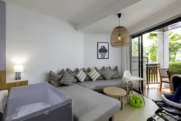 Hotelzimmer im Sunwing Kamala Beach mit L-förmigem Sofa, Nachttisch und Babystuhl.