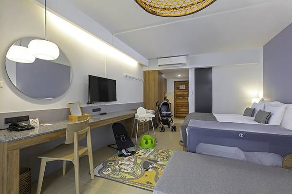 Innenansicht eines Hotelzimmers im Sunwing Kamala Beach mit Schreibtisch, Stuhl, Fernseher, Spiegel, Babystuhl und Kinderbett.