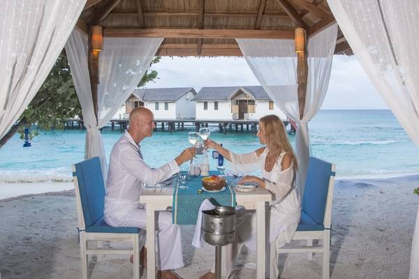 Paar beim Essen im Reethi Beach Resort mit Blick auf den Ozean und traditioneller Architektur