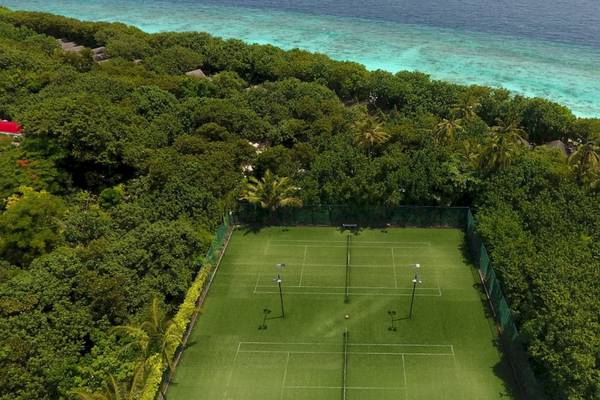 Luftaufnahme eines Tennisplatzes im Reethi Beach Resort, umgeben von Bäumen und Blick auf das Meer.