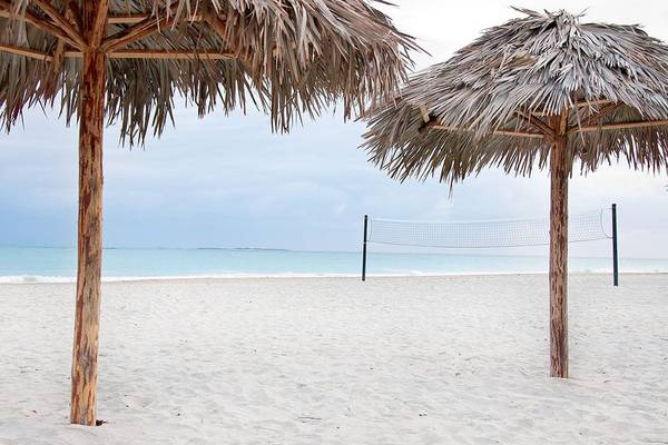 Zwei Strohschirme am Strand mit einem Volleyballnetz im Hintergrund.