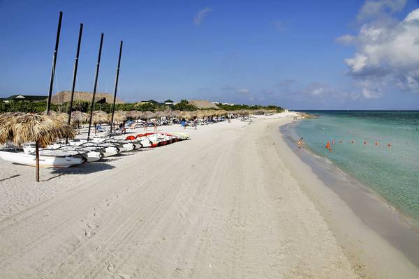 Foto einer weißen Sandstrand mit mehreren Booten und Strohhüten