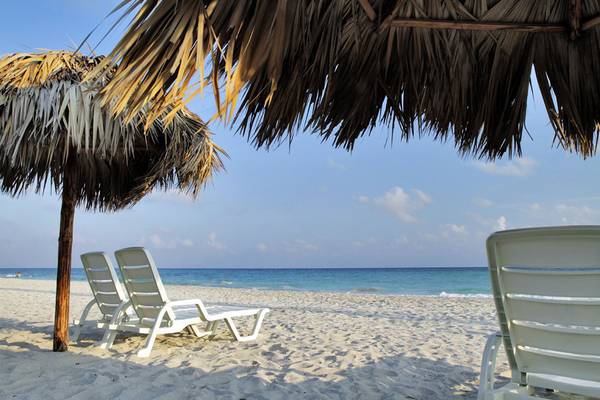 Strandszene mit Sonnenliegen unter Strohhüten im Valentin Varadero El Patriarca Hotel.