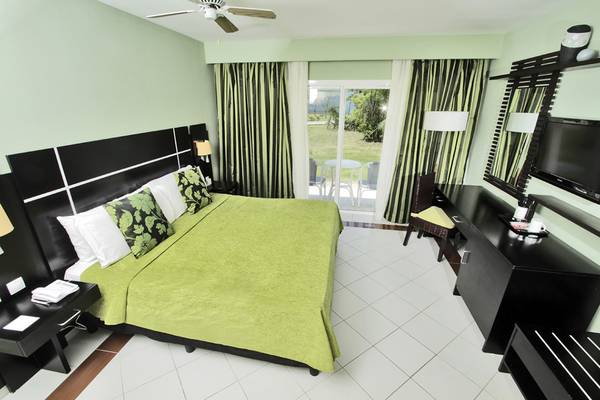 Ein modernes Hotelzimmer mit grünen Bettwäsche, weißem Boden und einer Terrassentür.