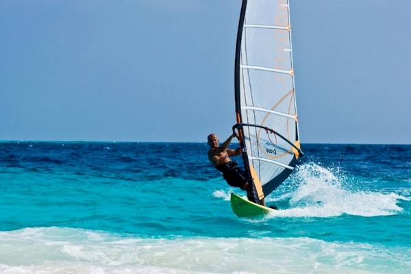 Ein Mann windsurft auf blauem Wasser im Meer bei Sonnenaufgang.
