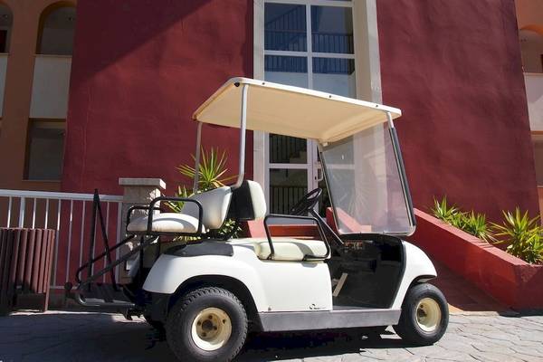 Ein weißer Golfwagen steht vor dem roten Gebäude des Hotels Bordoy Don Antonio.