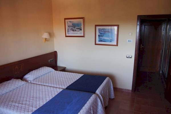 Doppelzimmer im Bordoy Don Antonio Hotel mit zwei Betten, Decken und Kissen, neben einer Wand mit zwei gerahmten Bildern und einer offenen Tür.