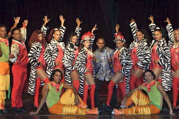 Eine Gruppe von Tänzern und Tänzerinnen in bunten Kostümen, die eine Show auf der Bühne des Grand Palladium Bavaro Suites Resort & Spa veranstalten.