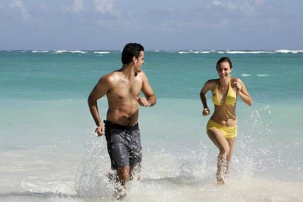 Ein Paar läuft am Strand, das Grand Palladium Bavaro Suites Resort & Spa ist im Hintergrund.