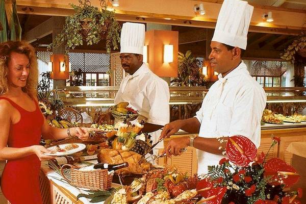 Ein Paar und ein Mann stehen vor einem Buffettisch mit Essen, serviert von Köchen im Grand Palladium Bavaro Suites Resort & Spa.