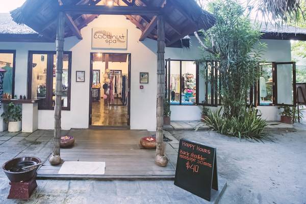 Das Reethi Beach Resort Coconut Spa mit einem Eingang, Pflanzen und einem Schild mit Öffnungszeiten.