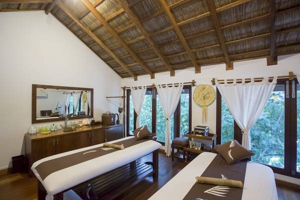 Spa-Zimmer mit zwei Massagebetten und Fenstern, die natürliches Licht hereinlassen.