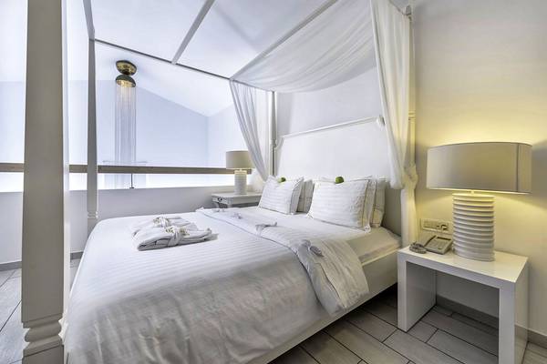 Innenansicht des Schlafzimmers im Diamond Deluxe Hotel mit vierposterbett, weißen Vorhängen und modernen Lampen.