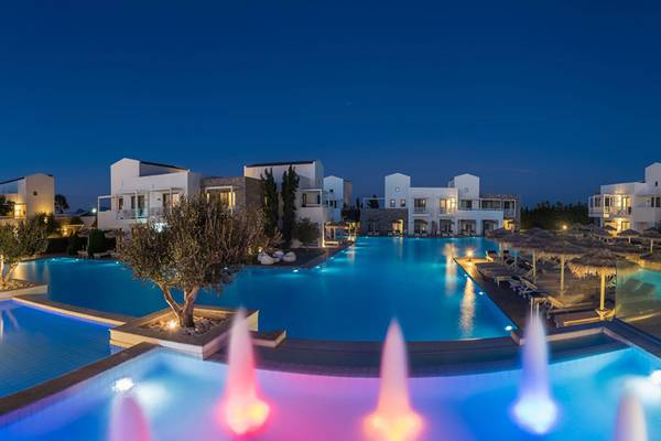 Ein Hotelpool bei Nacht mit farbigen Wasserfontaenen und umliegenden Villas