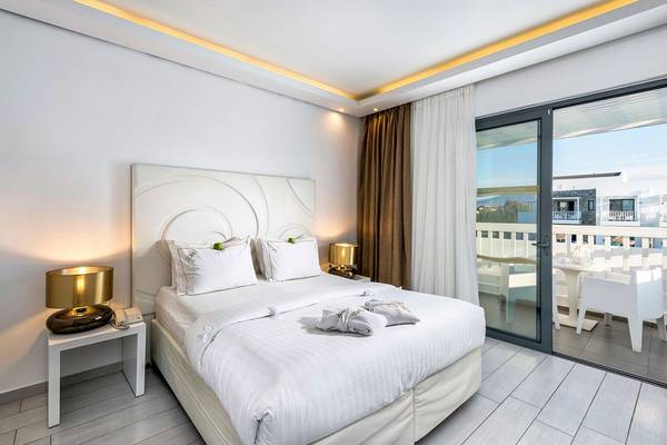 Schlafzimmer im Diamond Deluxe Hotel mit weißem Bett, Nachttischen und Balkon mit Tisch und Stühlen.