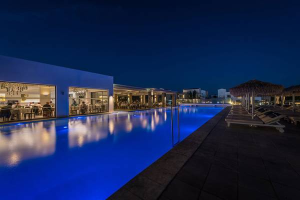 Der Pool des Diamond Deluxe Hotels bei Nacht mit Gästen, die drinnen sitzen und Sonnenliegen draußen.