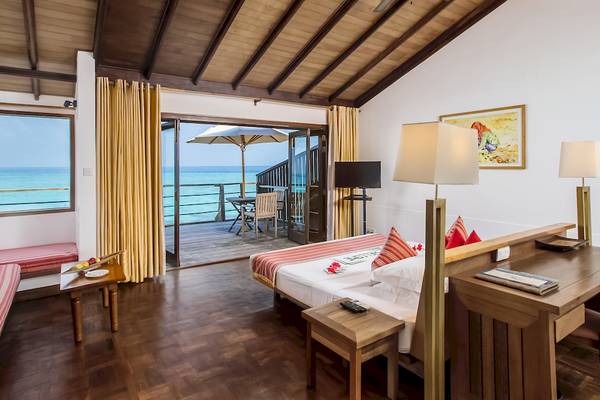 Innenansicht eines Zimmers im Reethi Beach Resort mit Meerblick, Doppelbett, Schreibtisch und Balkon mit Tisch und Stühlen.