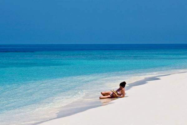 Eine Frau liest auf dem weißen Sandstrand des Reethi Beach Resorts.