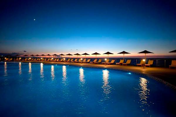 Der Swimmingpool des Royal Blue Resorts bei Nacht mit Sonnenliegen und Sonnenschirmen.