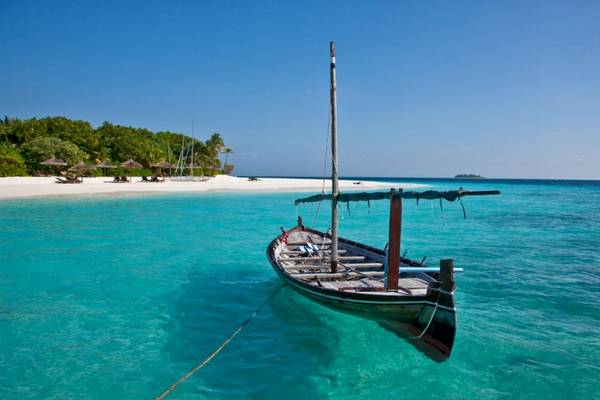 Ein Boot am Strand im Reethi Beach Resort mit einer weißen Insel im Hintergrund.