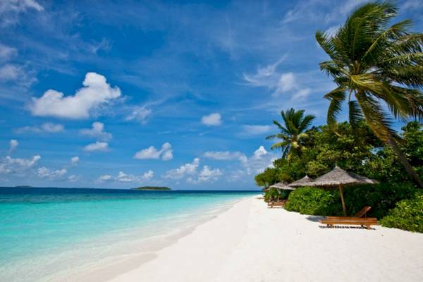 Sonnenstrand mit weißen Palmen, Lounge-Stuhl und Sonnenschirm im Reethi Beach Resort.