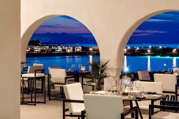 Außenrestaurant des Knossos Beach Bungalows Suites Resort & Spa bei Nacht mit Blick auf das Meer und die Stadt.