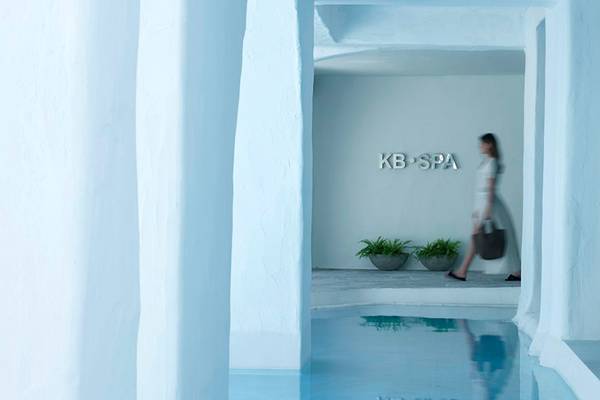 Eingang des Knossos Beach Bungalows Suites Resort & Spa mit Frau und KB SPA Schild