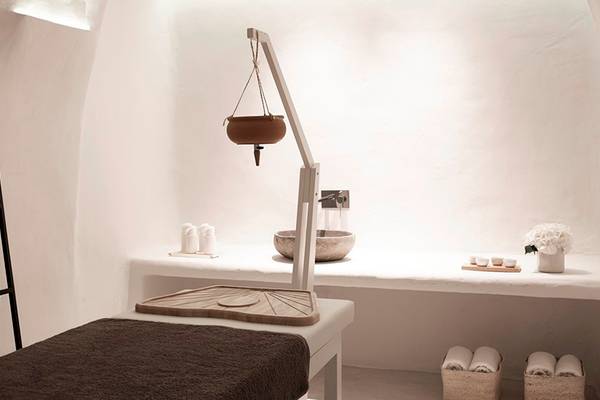 Massageraum im Knossos Beach Bungalows Suites Resort & Spa mit weißen Wänden, einer Massageliege und einem Tisch mit Waschbecken.