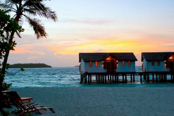 Zwei Wasservillen des Reethi Beach Resorts am Strand bei Sonnenuntergang.