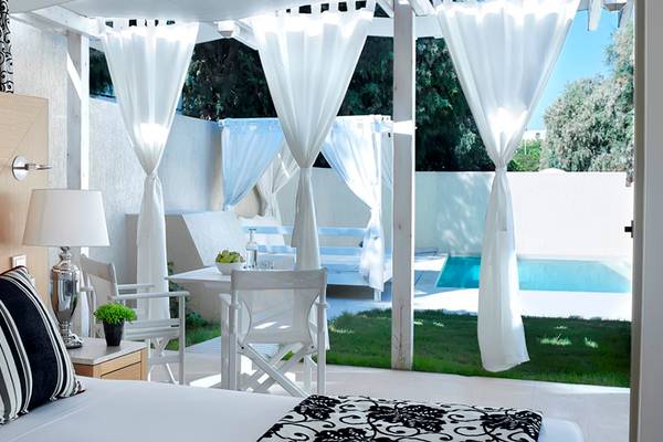 Hotelzimmer mit Aussicht auf Pool und Außenbereich mit weißen Möbeln und Vorhängen.