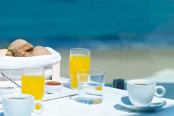 Frühstück am Strand im Knossos Beach Bungalows Suites Resort & Spa mit Orangensaft, Kaffee und Gebäck.