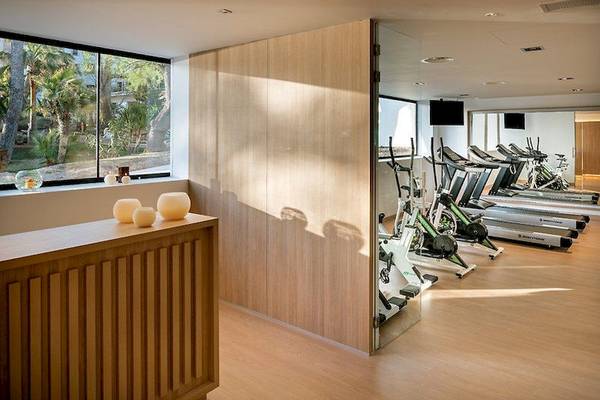 Fitnessraum im Secrets Mallorca Villamil Resort & Spa mit Laufbändern und Blick auf den Garten.