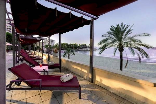 Strand-Lounge-Bereich im Secrets Mallorca Villamil Resort & Spa mit roten Liegen und Sonnenschirmen.