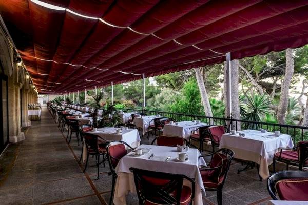 Terrasse des Secrets Mallorca Villamil Resorts & Spa mit vielen Tischen und Stühlen unter einem roten Vordach.