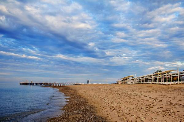 Arcanus Side Resort Strand mit Pier unter wolkigem Himmel.