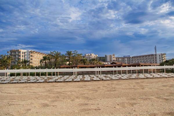 Außenbereich des Arcanus Side Resort Hotels mit weißen Sonnenliegen auf sandigem Strand.