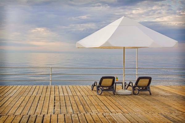 Terrasse des Arcanus Side Resort mit zwei Sonnenliegen unter einem weißen Schirm und Blick auf das Meer.