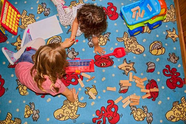 Zwei Kinder spielen mit Holzsteinen auf einem bedruckten Teppich.
