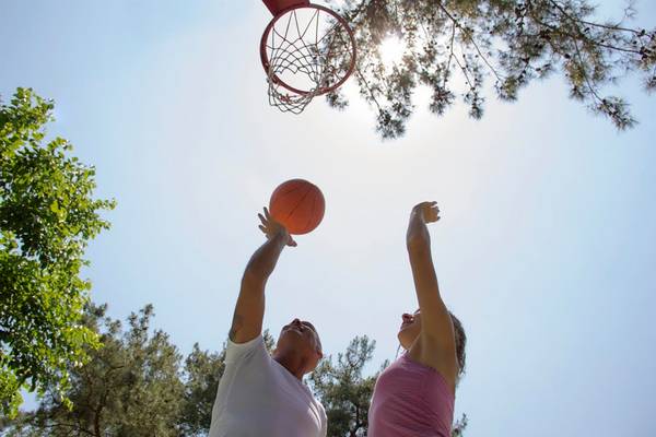 Ein Mann und eine Frau spielen Basketball unter einem Baum im Freien.